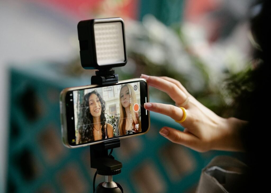 Two women recording a video using a smartphone and LED light setup, illustrating modern content creation.