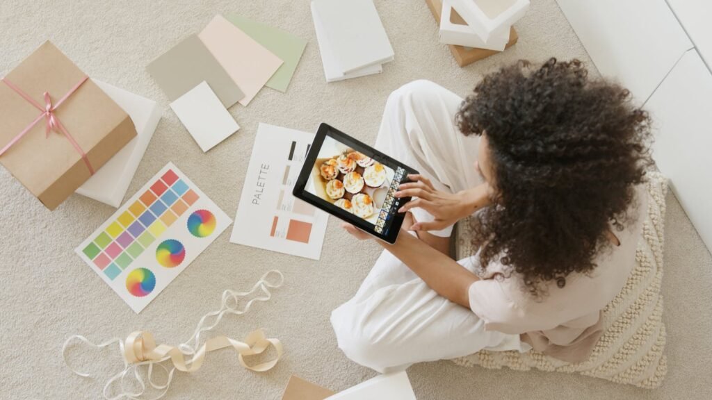 Woman using tablet surrounded by design tools and gift box, showcasing creativity and online work.